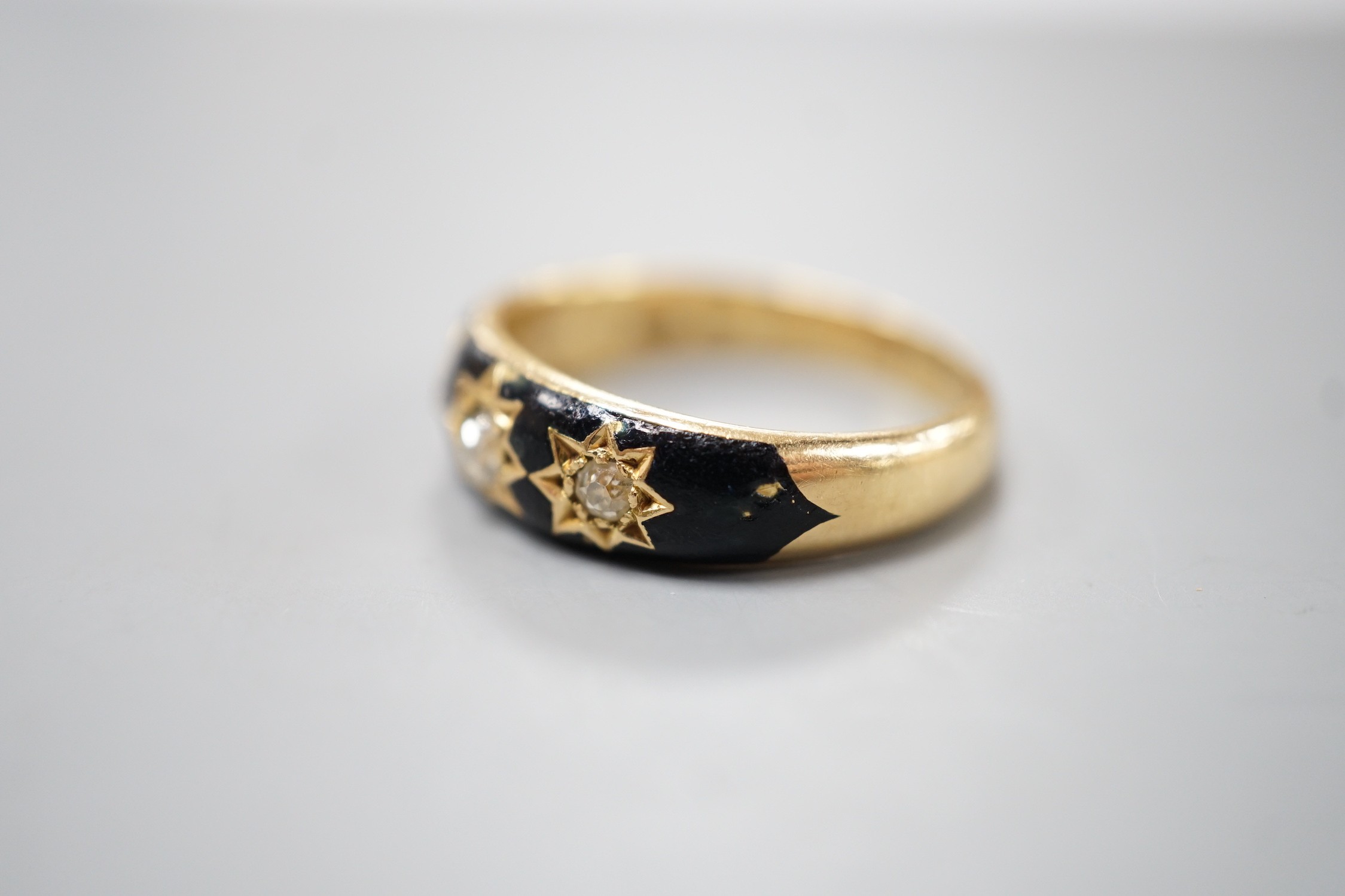 An Edwardian 18ct, black enamel and three stone gypsy set diamond mourning ring, size Q/R, gross weight 6.6. grams, the interior shank inscribed 'Sacred to the memory of my beloved husband'.